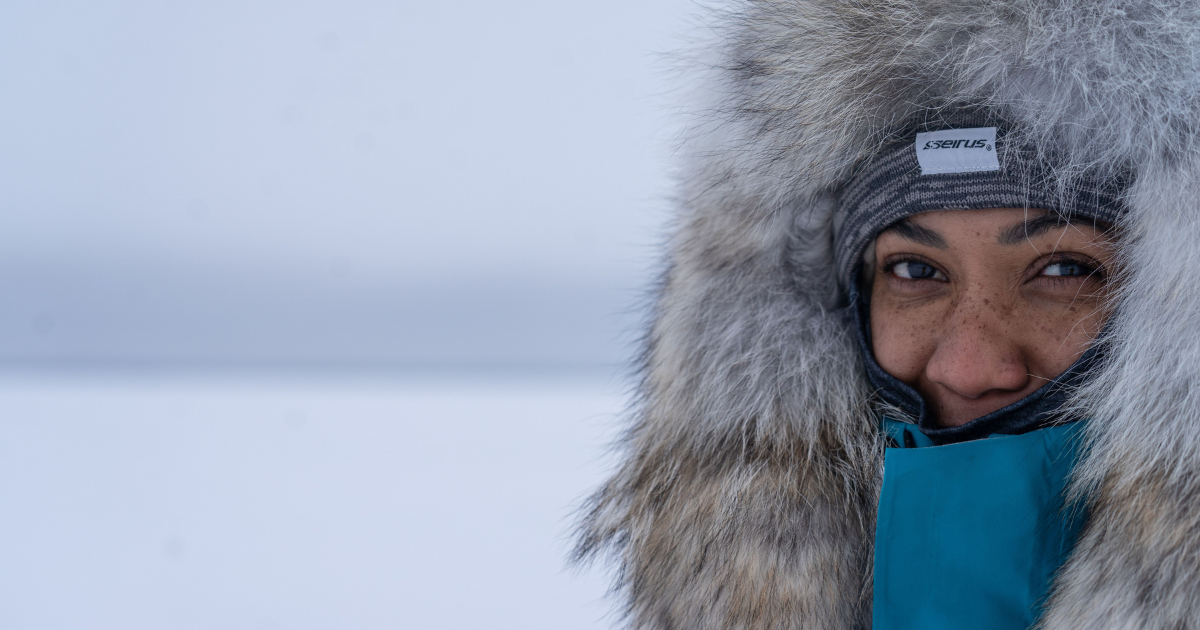 A woman wearing a heavy winter jacket with a fur-lined hood and a beanie, looking protected from sub-zero temperatures.