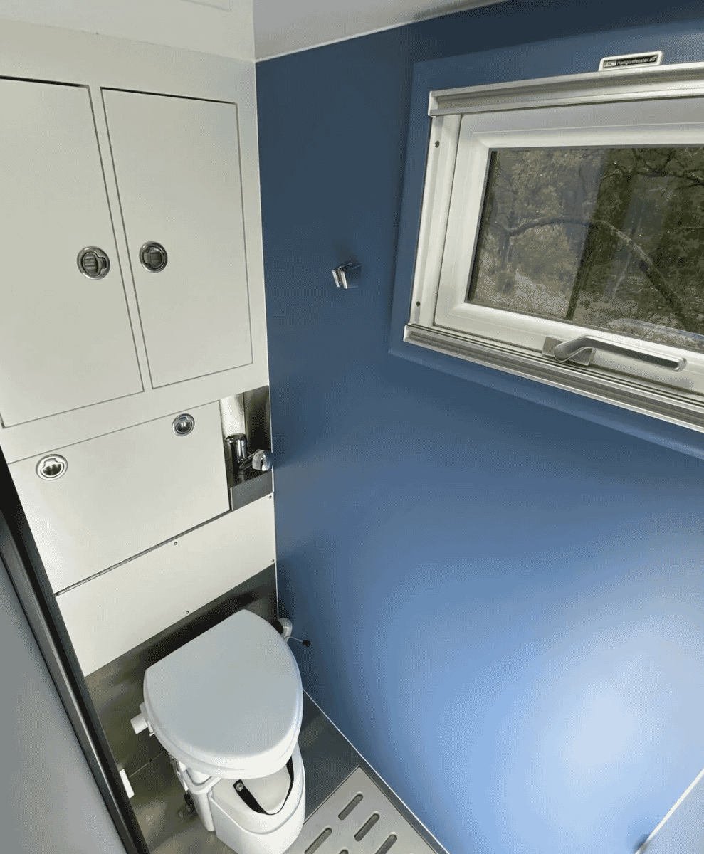 A modern compact bathroom inside the vehicle with deep blue walls and sleek white fixtures.