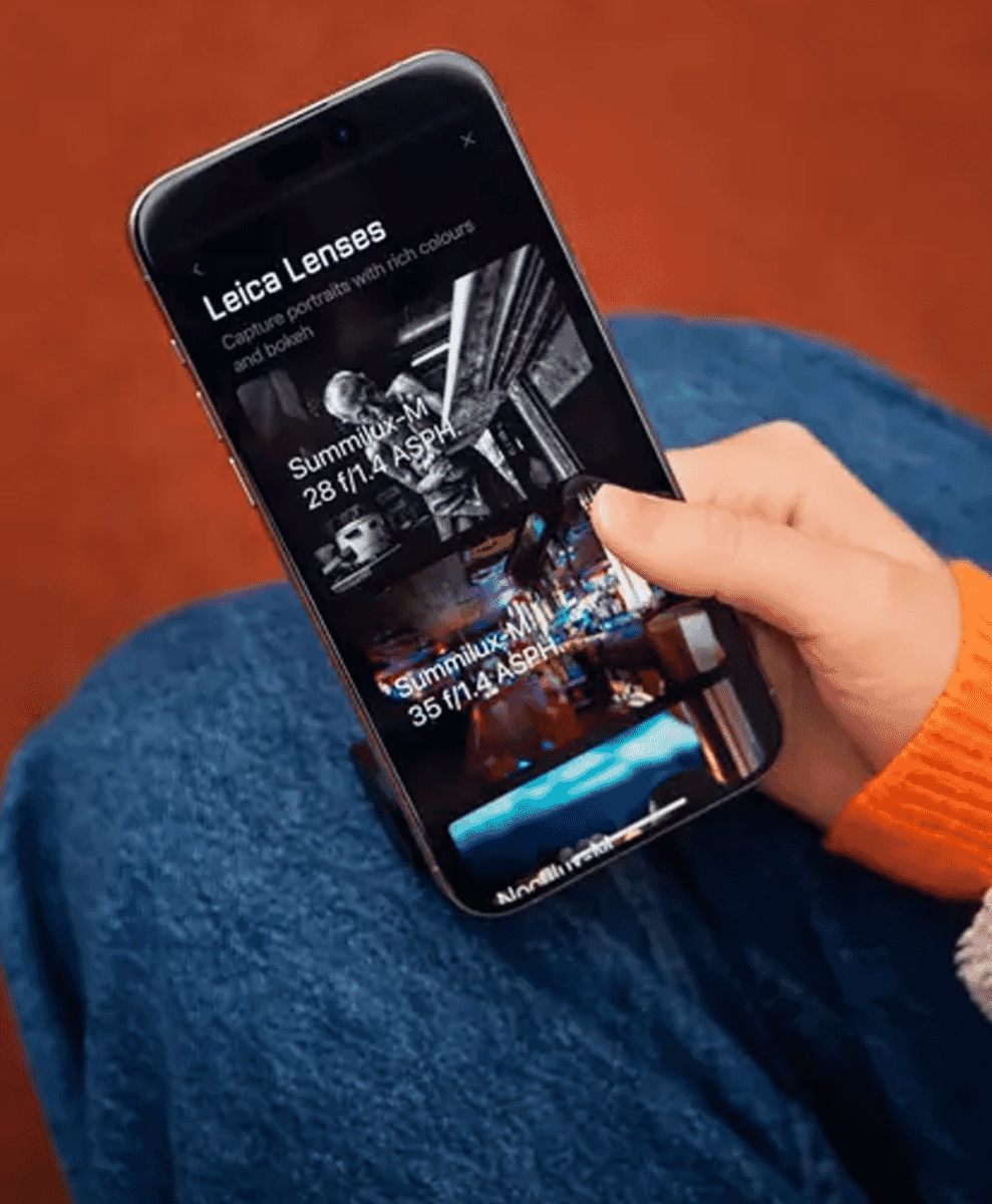 A smartphone screen displaying the Leica LUX Pro app lenses held by a person in a blue and orange outfit.