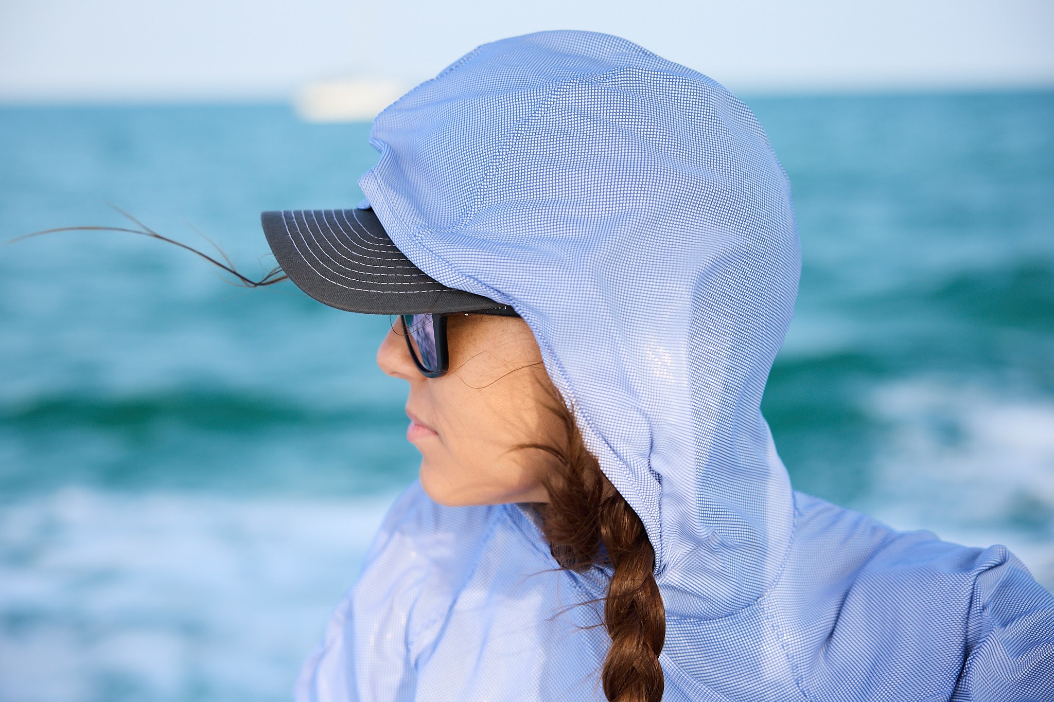 An angler fishing from a boat deck under intense direct sunlight reflecting off the water.