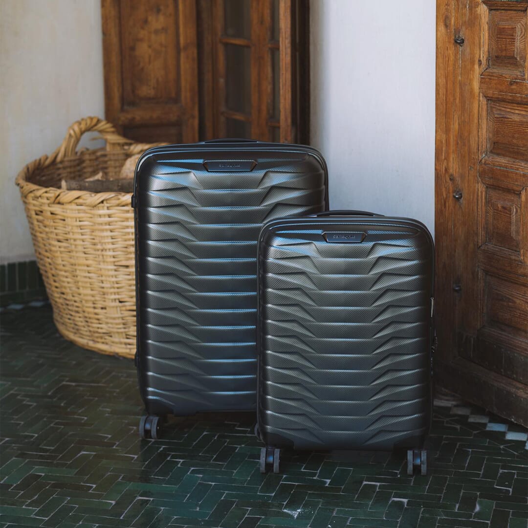 Two black Samsonite hard-shell suitcases with zigzag patterns on a green herringbone tile floor.