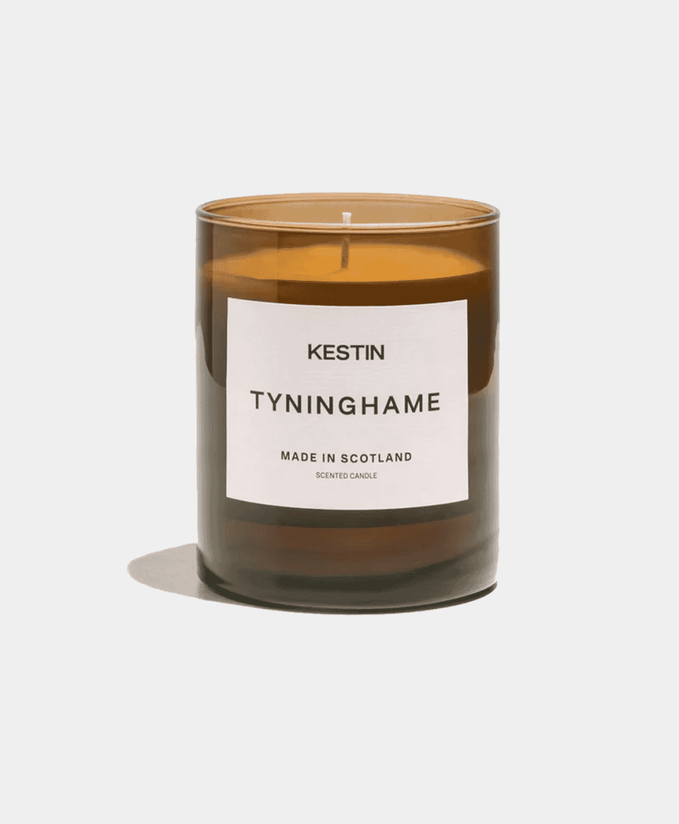 A Tyninghame scented candle in an amber glass jar against a white background.