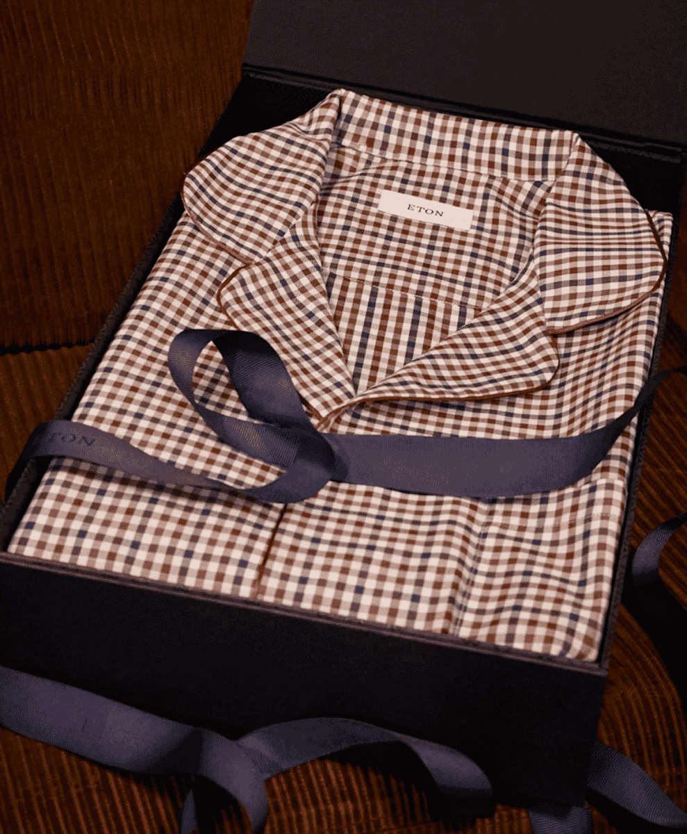 A folded ETON gingham pajama top presented inside a premium black gift box with a navy ribbon.