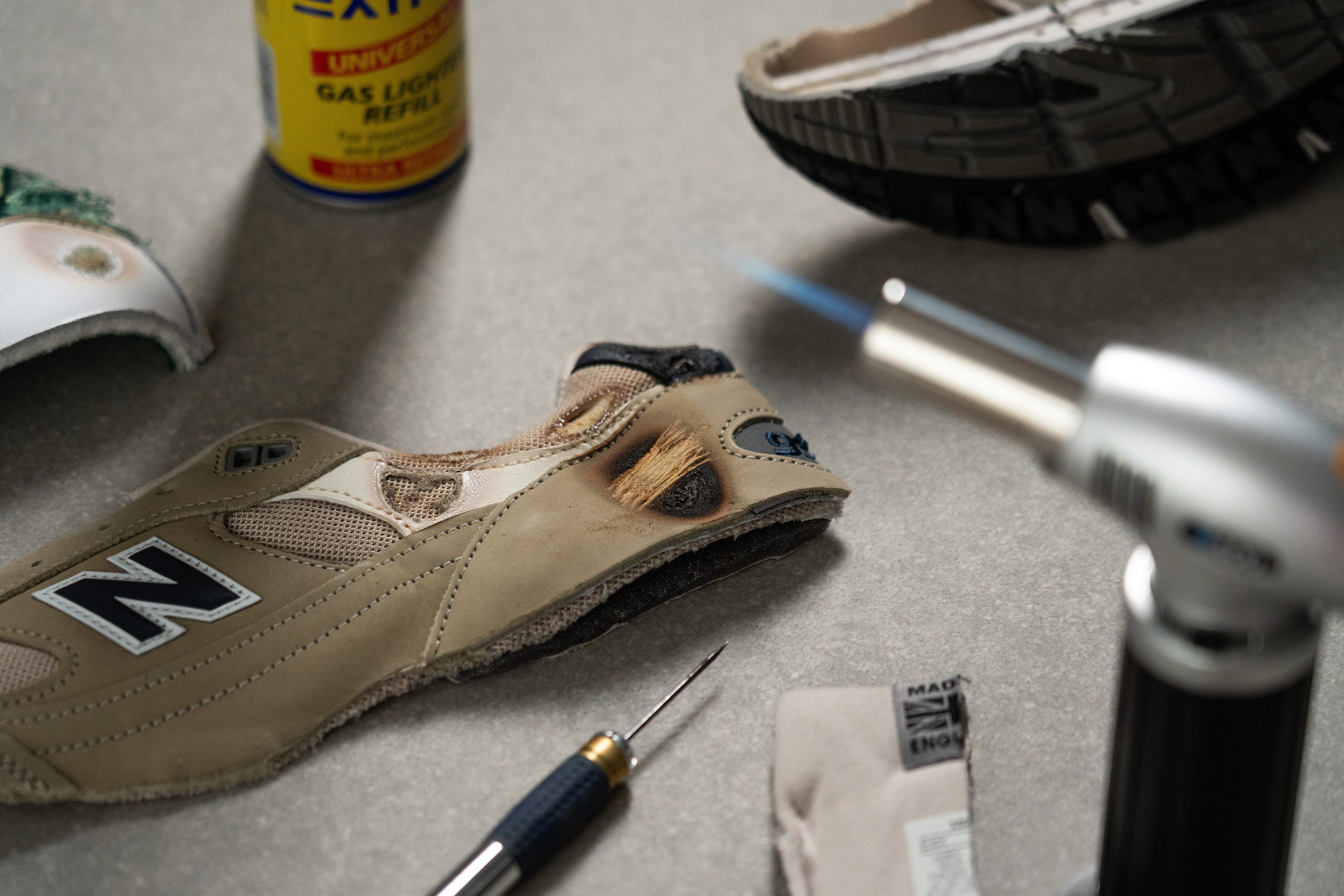 A lab technician using a butane torch to test the authenticity of the leather on a shoe upper.