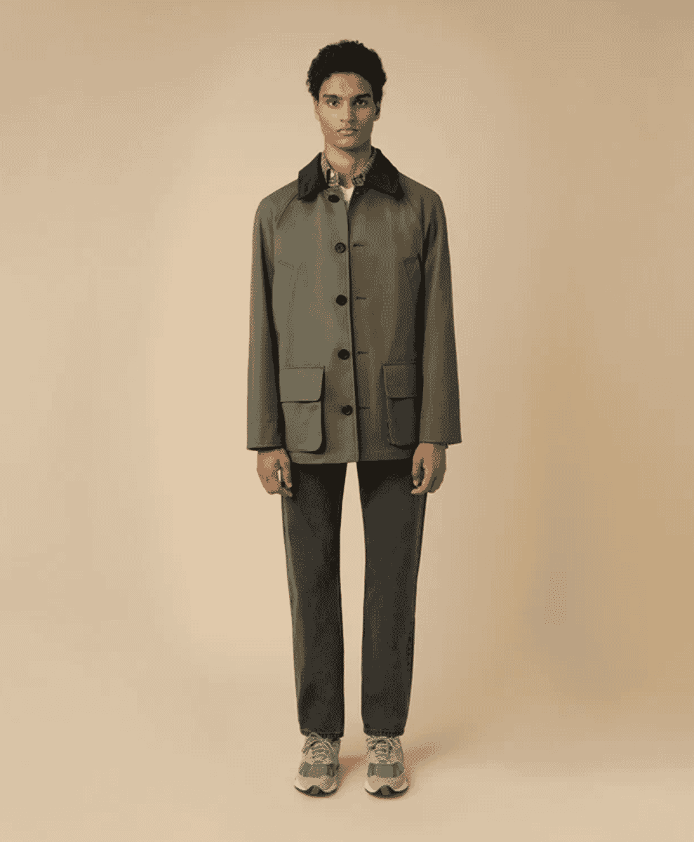 A man modeling a brown barn-style jacket over dark trousers in a clean studio setting.