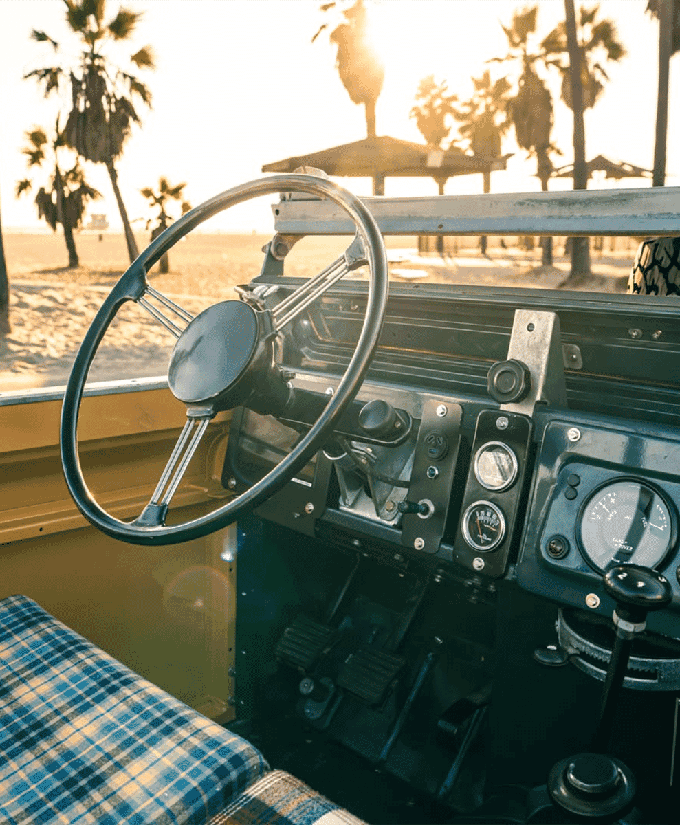 Interior view of a Land Rover featuring blue plaid seat covers and a beach view in the background.