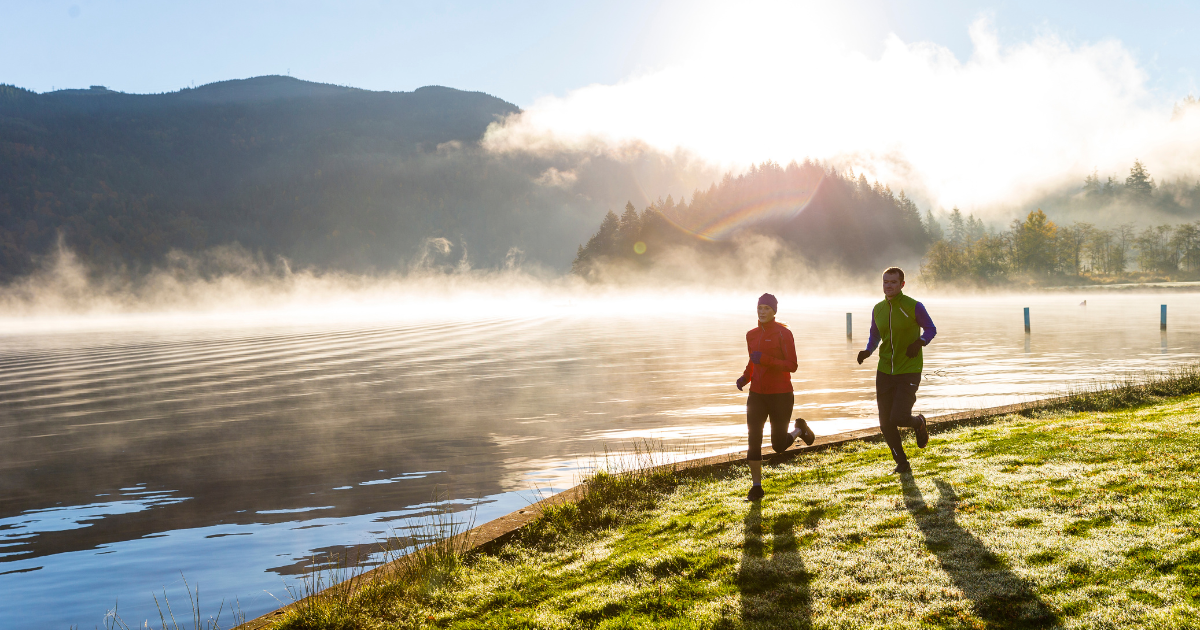 A man and woman running outdoors in cool weather wearing athletic winter gear.