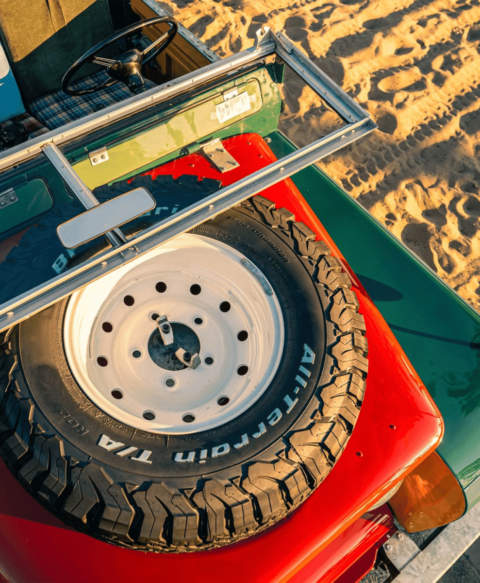 Close-up of a red and green vintage off-road vehicle's front panel and tire on a sandy beach.