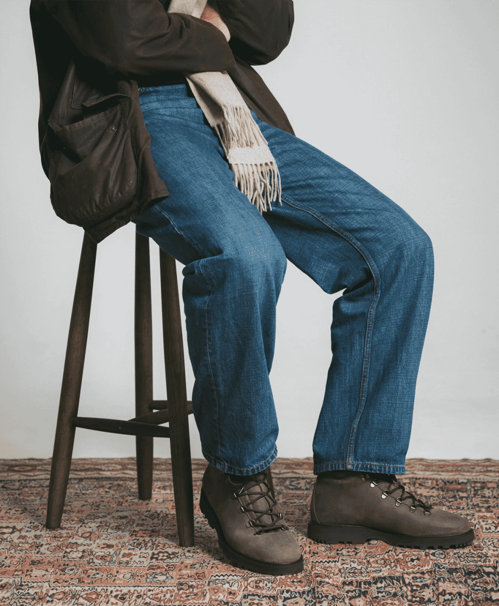 A man seated on a stool wearing a brown jacket, denim, and Myrqvist suede boots.