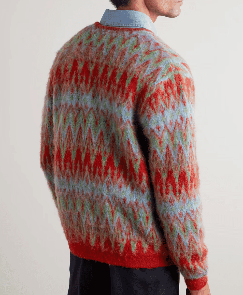 Close-up of a man wearing a red, green, and blue zigzag patterned fuzzy cardigan.