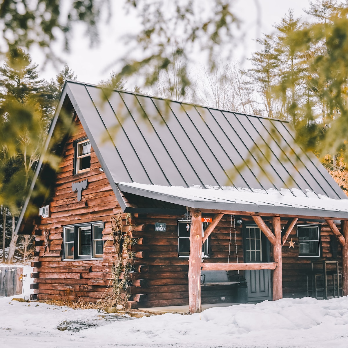 A small rustic log cabin surrounded by deep snow and tall pine trees.