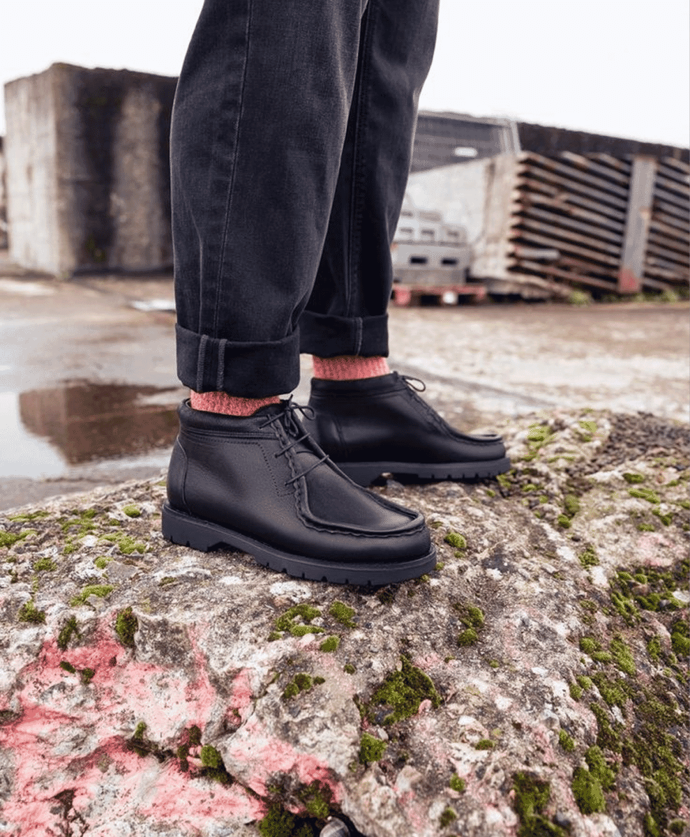 Black chunky boots worn with pink socks on a mossy rock.