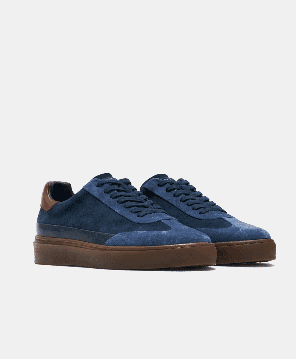 A pair of navy blue suede low-top sneakers with brown rubber soles on a white background.