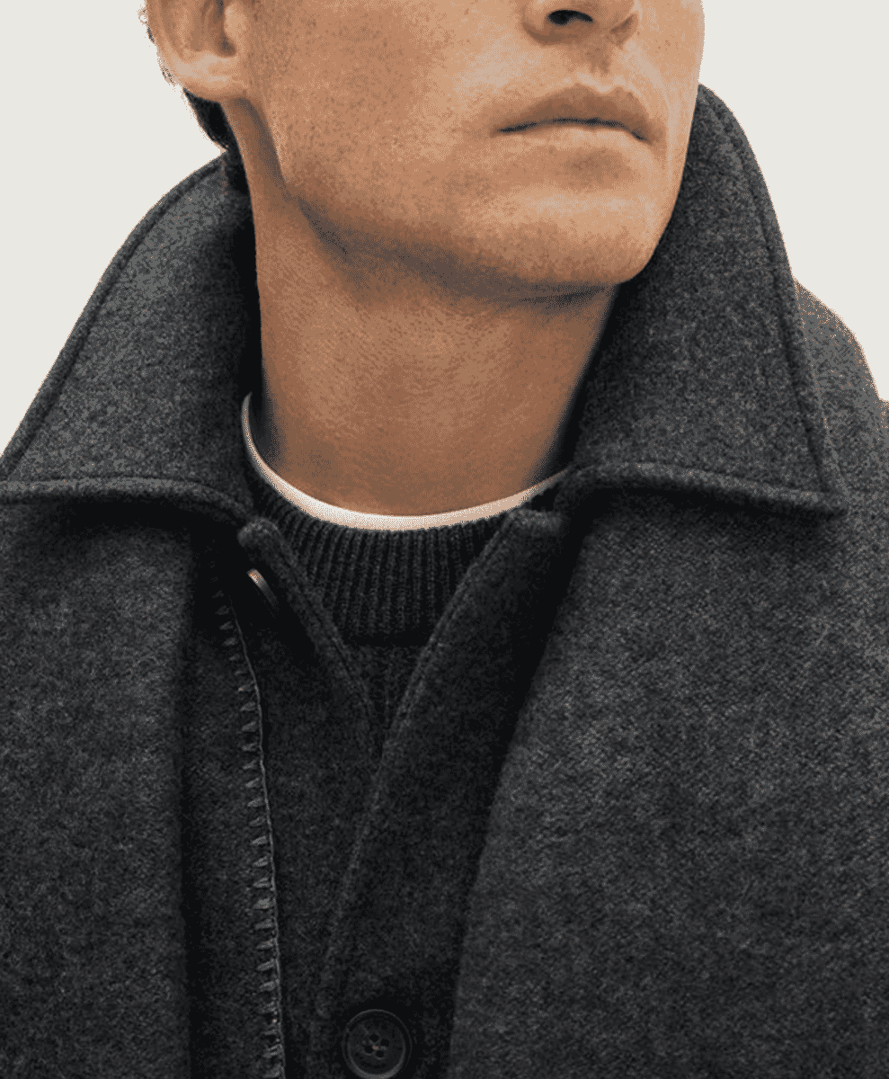 Close-up of a dark gray wool coat layered over a black ribbed sweater.