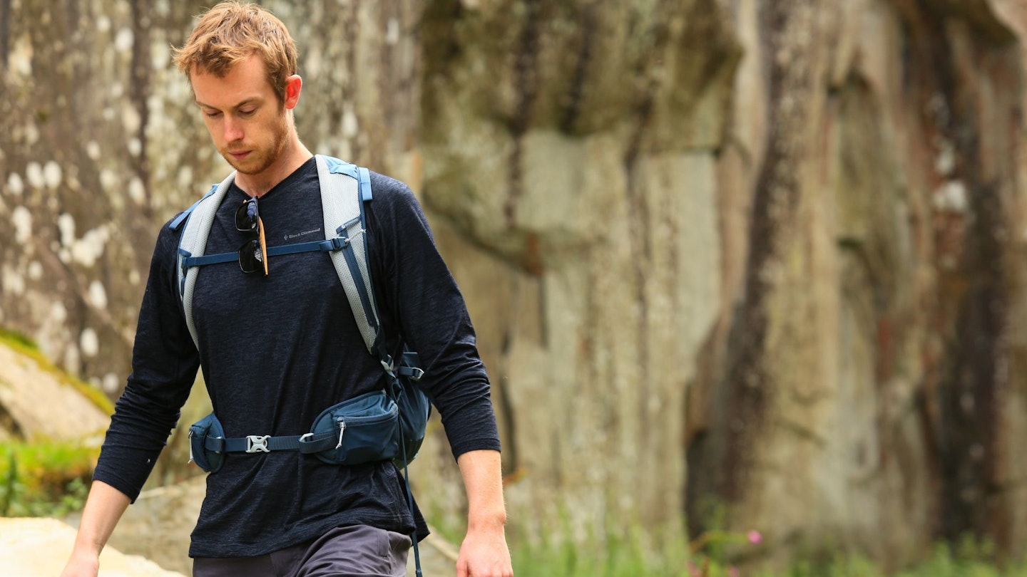 A hiker wearing a grey merino wool base layer top in an outdoor setting.