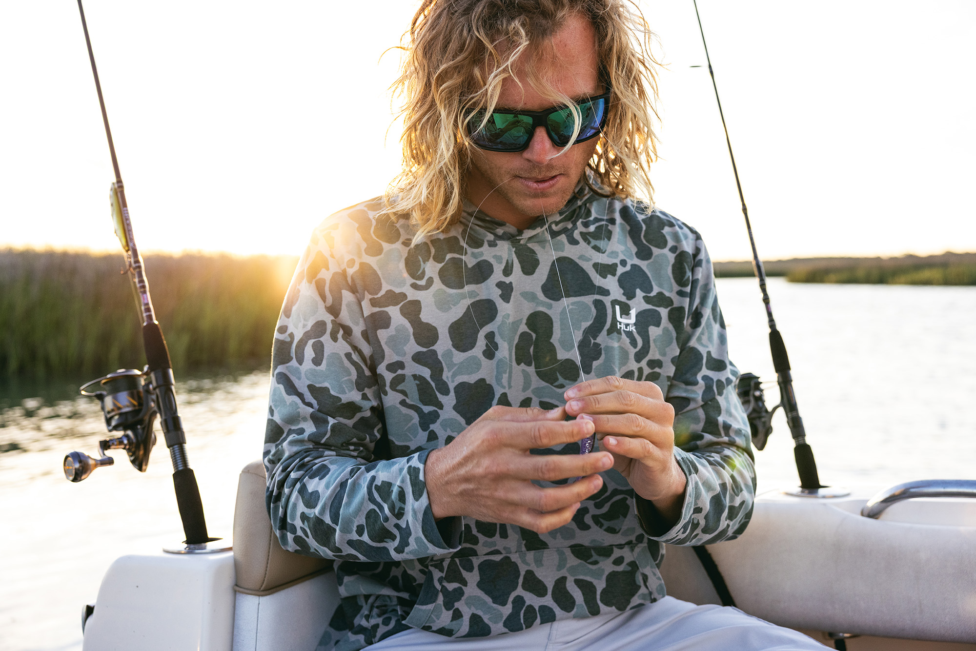 An angler on a boat wearing a grey HUK Leeward Fleece Hoodie.