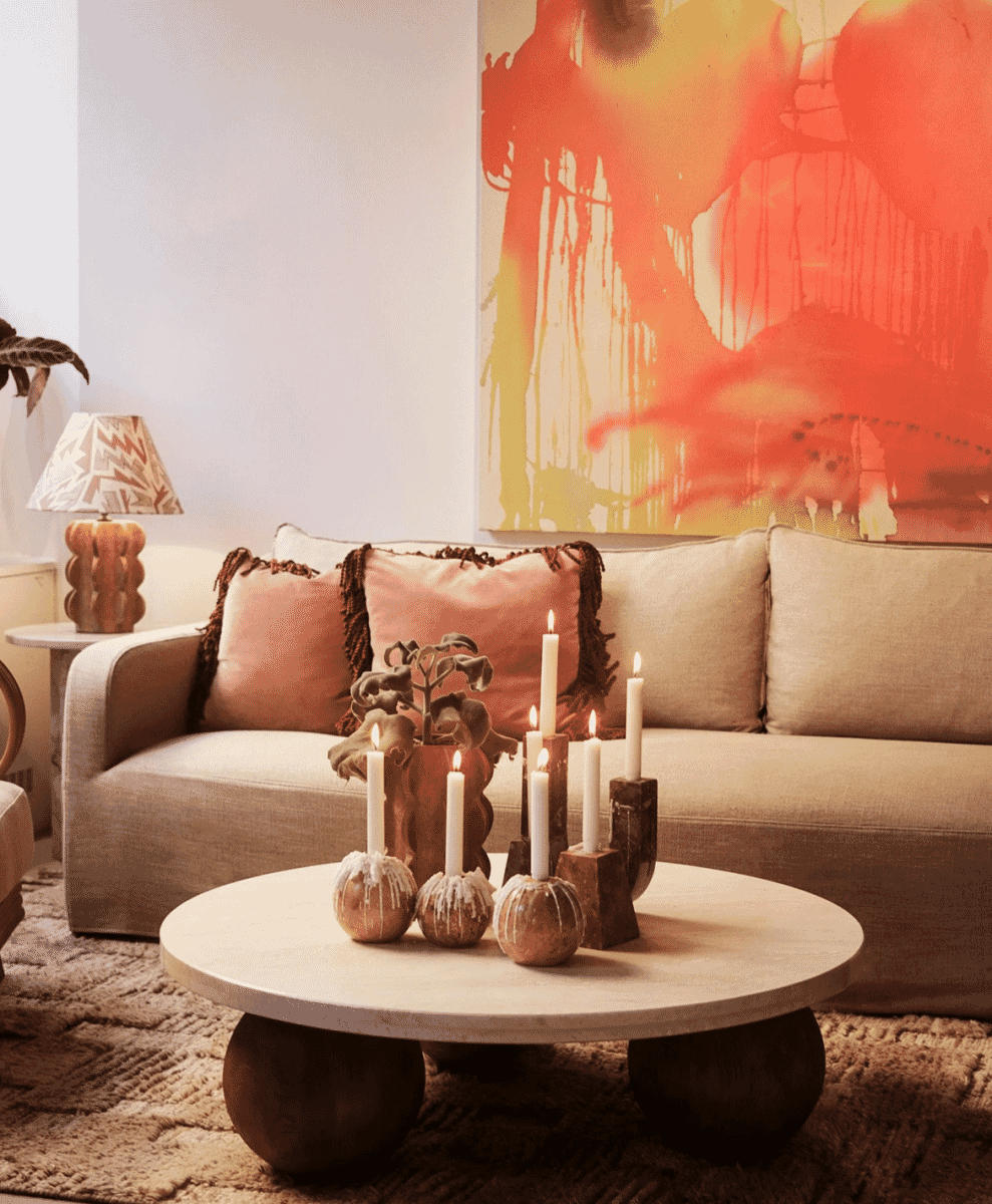 Cozy living room with a beige sofa, pink fringed pillows, and warm ambient lighting from candles.