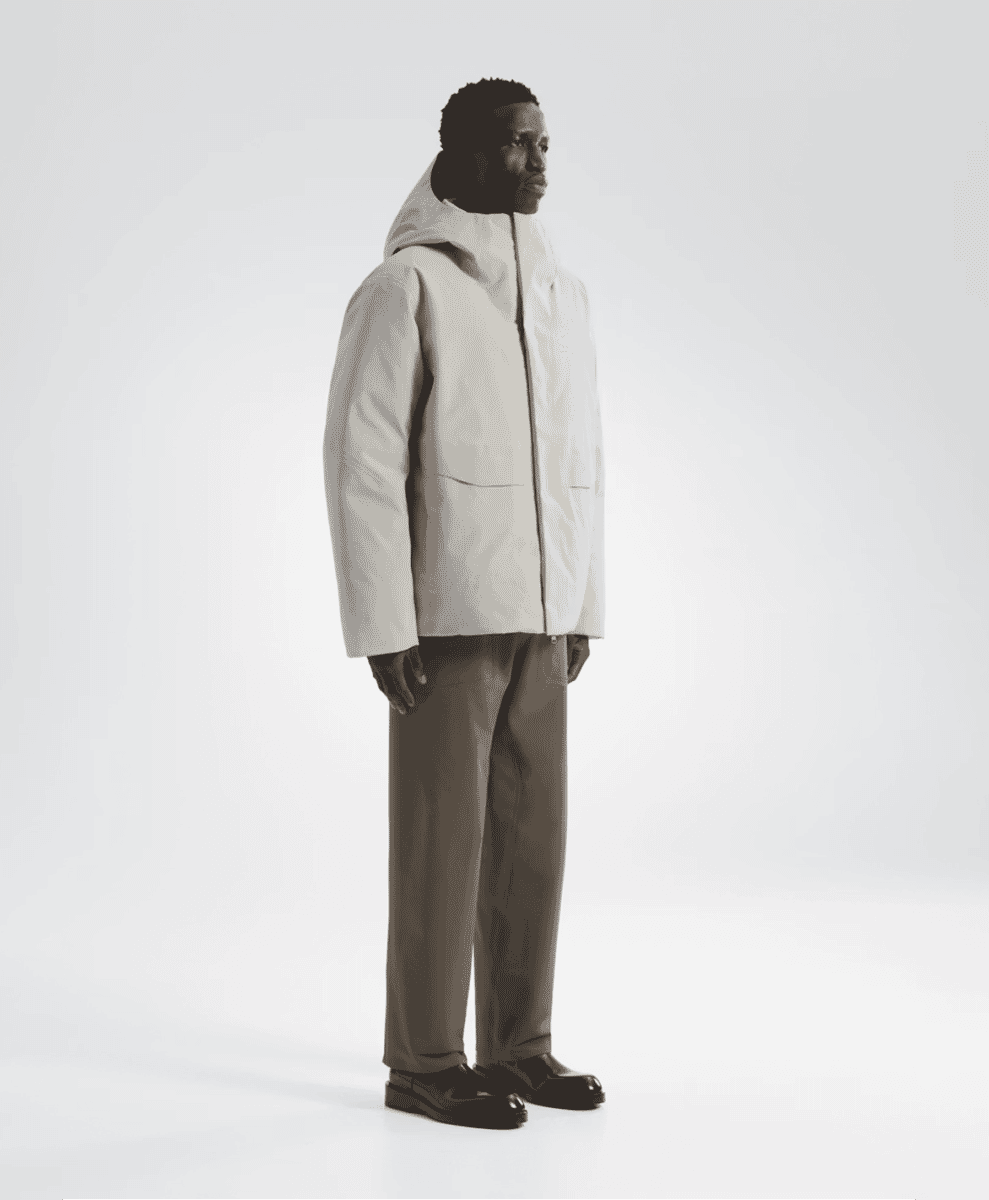 Profile view of a man in a white minimalist puffer coat and dark trousers.