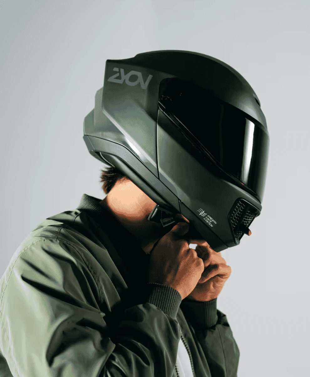 A man wearing a futuristic black motorcycle helmet with industrial branding.