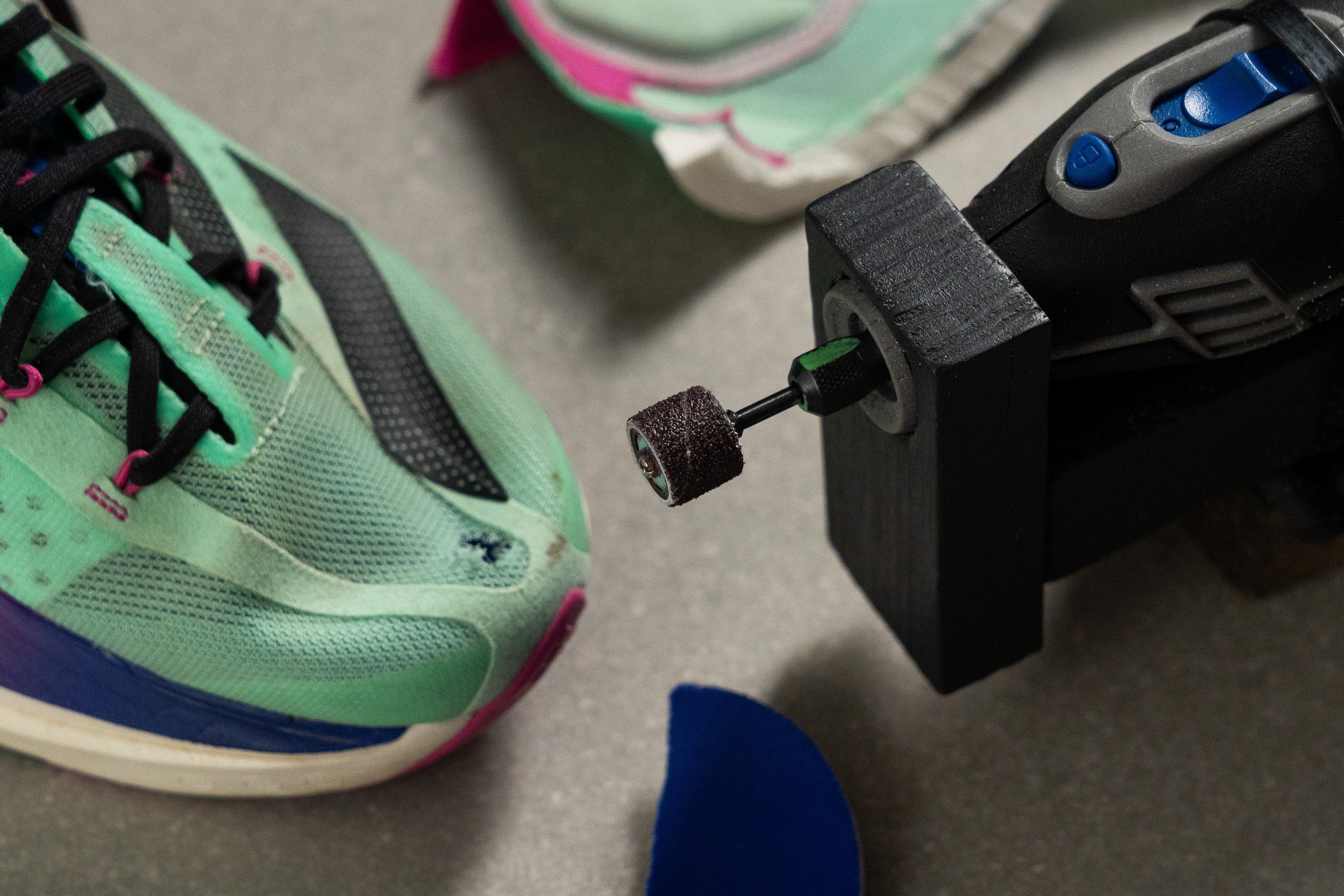 A motorized Dremel tool being applied to the toebox of a skate shoe in a lab setting.