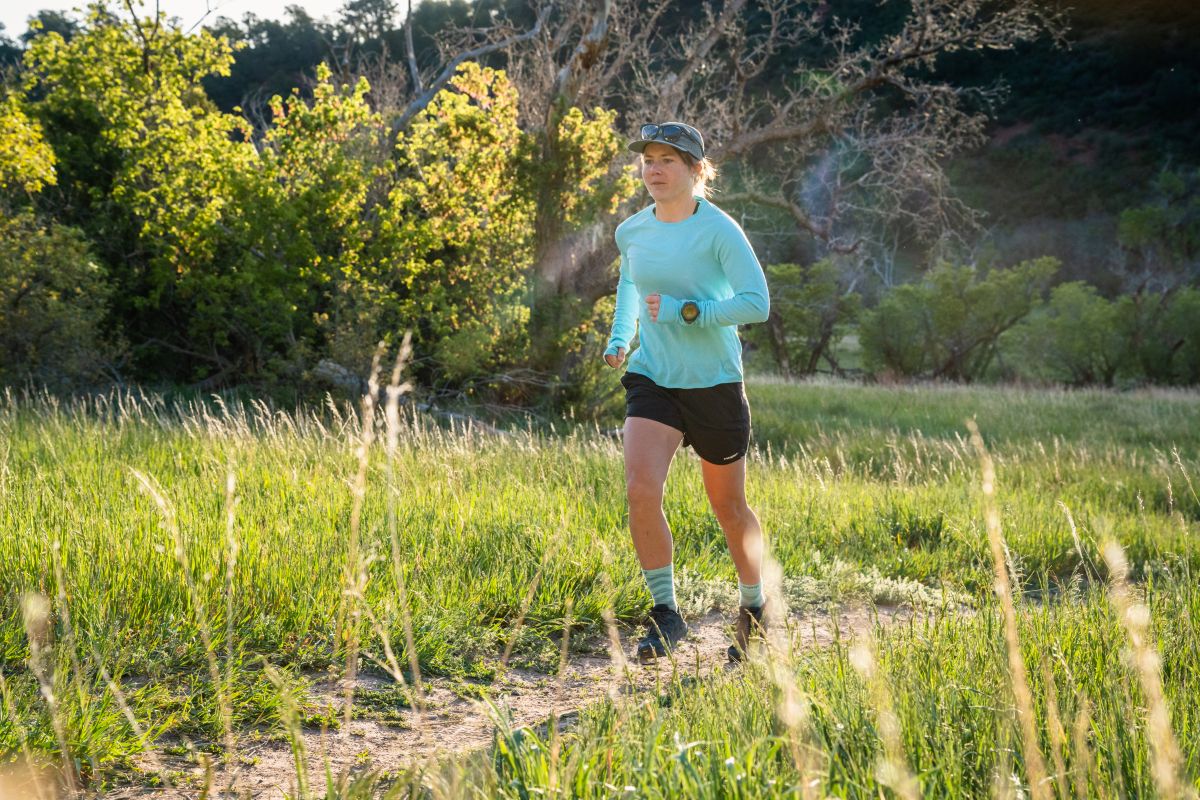 A runner traversing a sunlit grassy trail representing road-to-trail conditions.