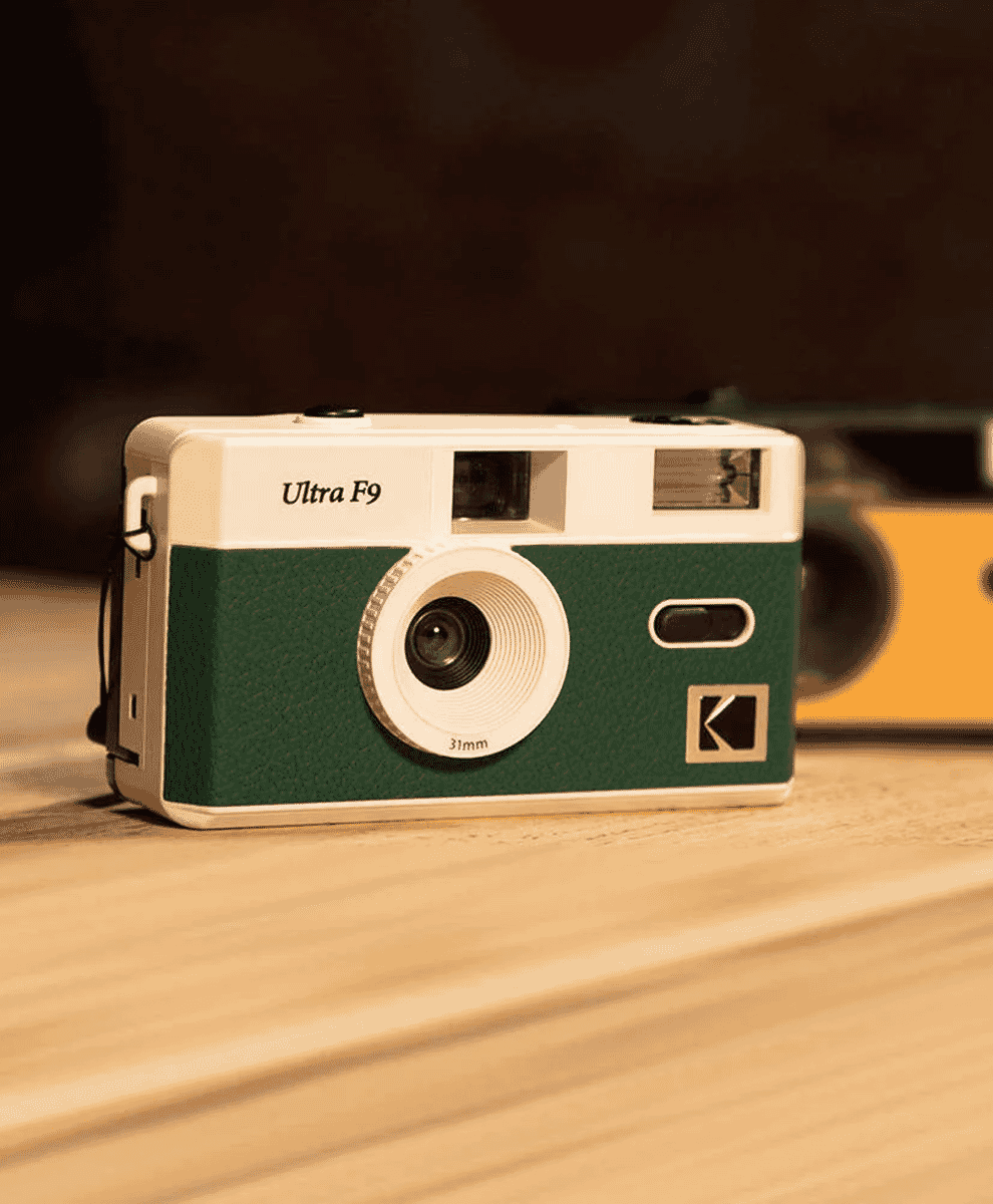 A green and white Kodak Ultra F9 film camera sitting on a wooden surface.
