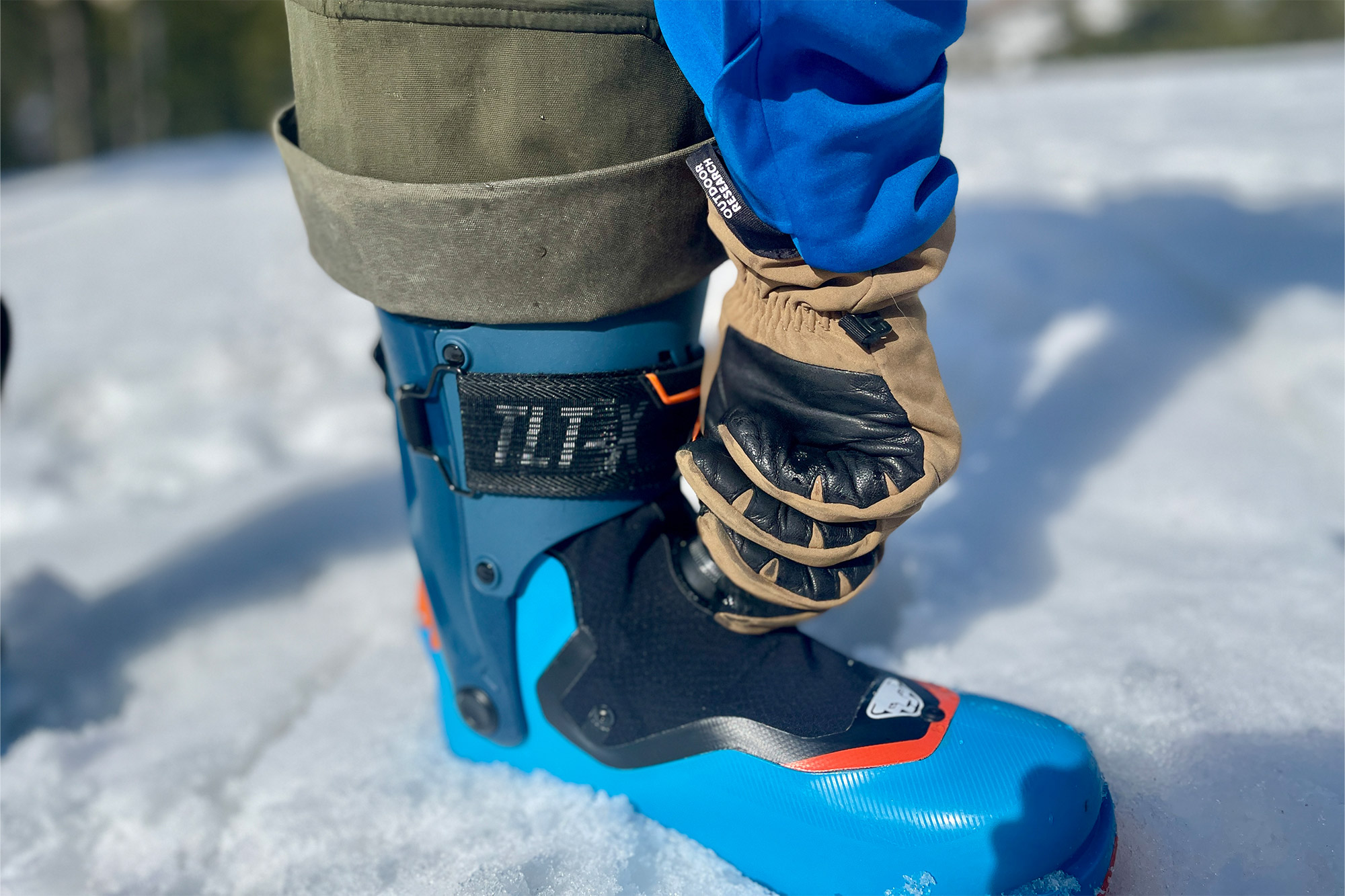 Close-up of a hand adjusting the orange Twistfit dial on the lower shell of a Dynafit ski boot.