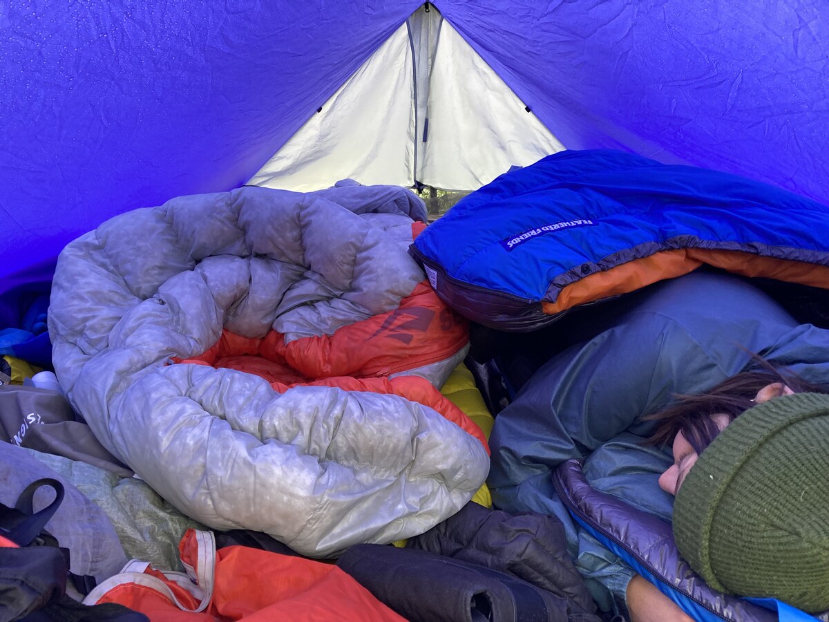 Two ultralight sleeping bags laid out under a tarp during a rainy night.
