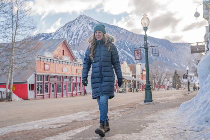A woman wearing the long Rab Deep Cover Down Parka in a snowy setting.