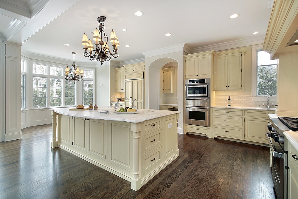 Ornate chandeliers hanging over a marble kitchen island with bright recessed ceiling lights.