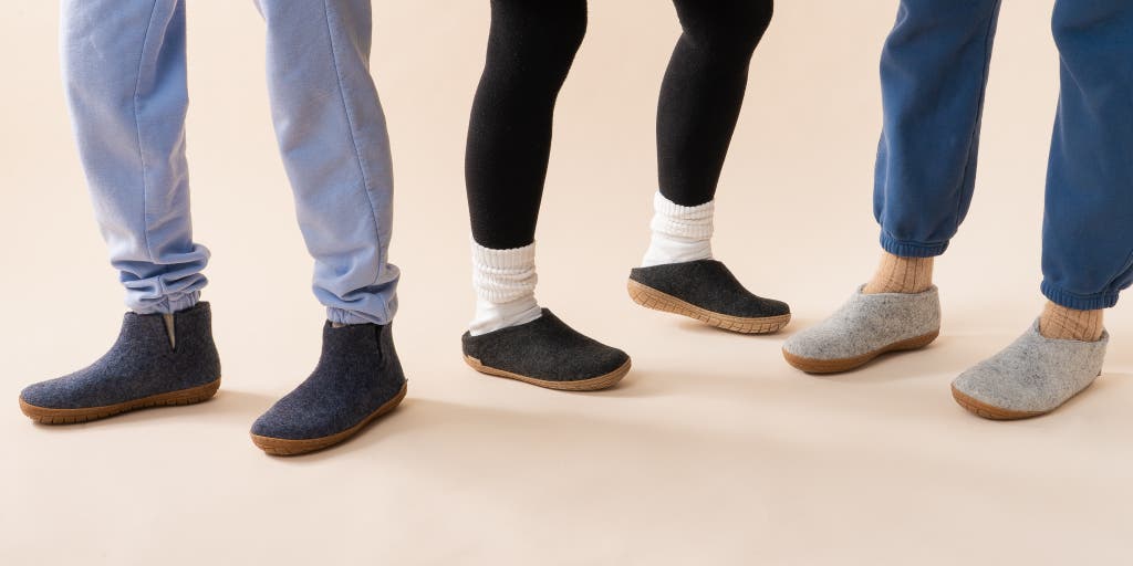 Three people sitting together wearing different styles of wool slippers including boots and slip-ons.