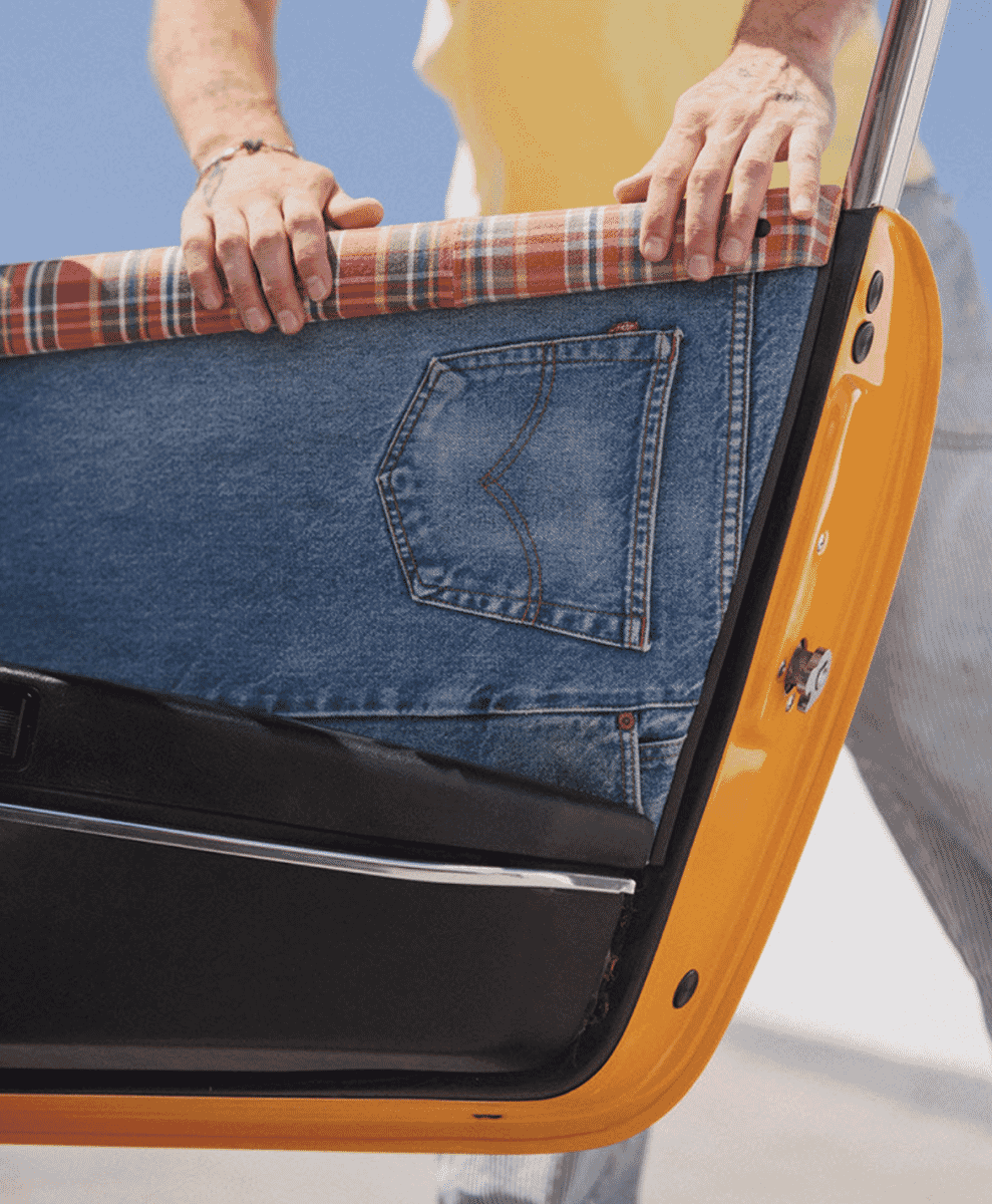 A person uses blue denim jeans as a car door liner with plaid fabric trim.