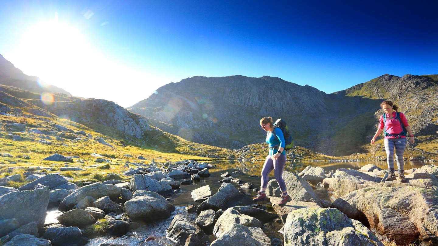 Two female hikers walking on a scenic trail wearing long-sleeve base layers.