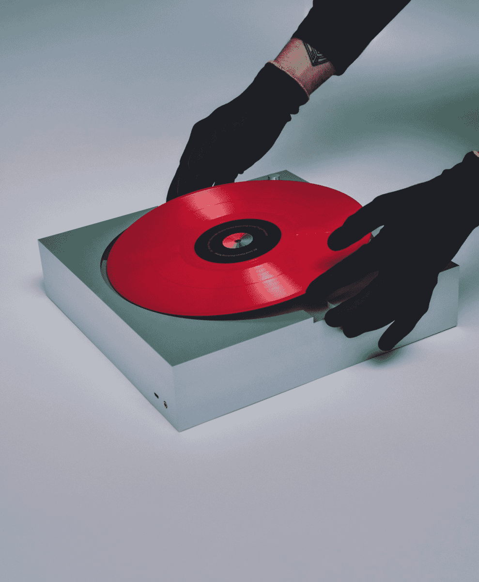 Close-up of a person in black gloves placing a red vinyl record onto a turntable.