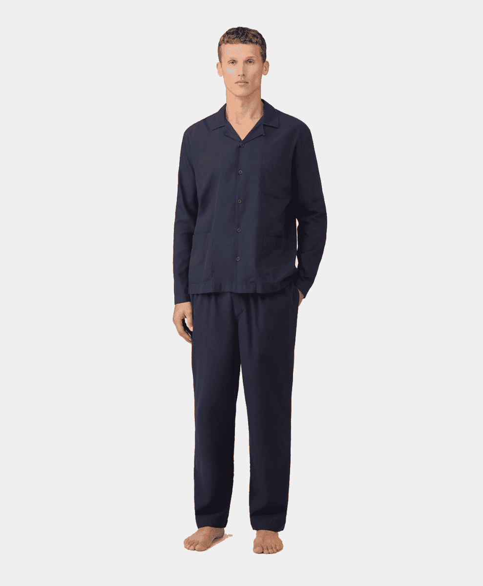 A man modeling a navy blue long-sleeve pajama set with a button-front shirt and matching trousers.