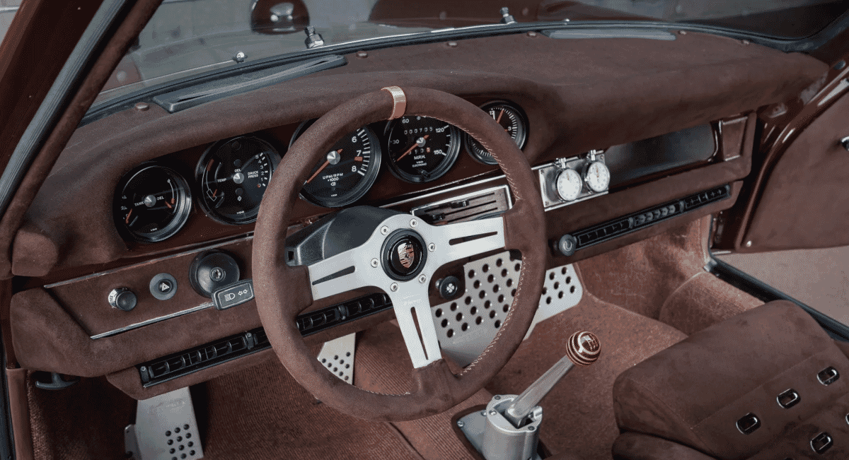 Interior of a classic Porsche featuring brown suede upholstery and a custom steering wheel.