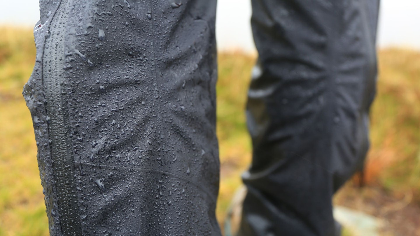 Macro photograph of clear water droplets beading up on a grey waterproof fabric surface.