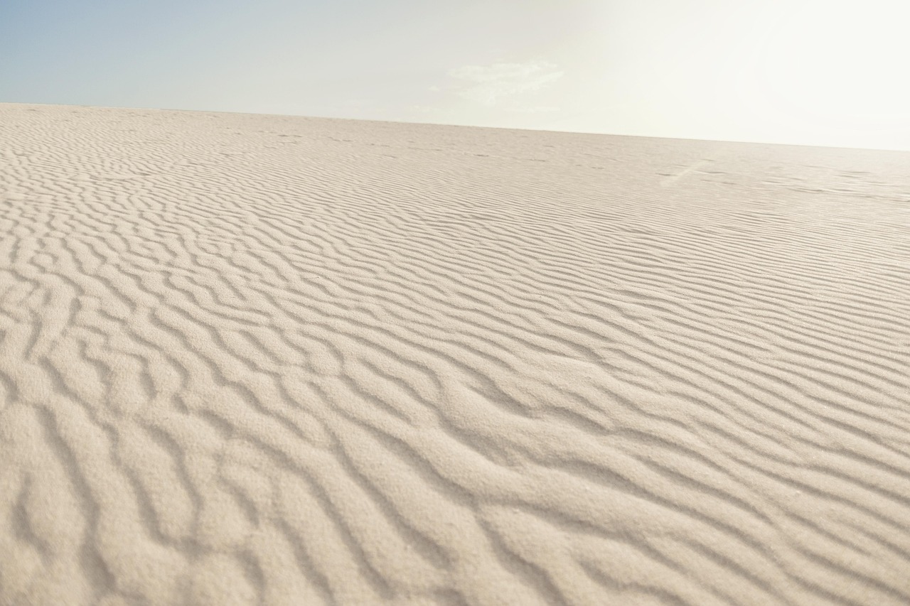 A minimalist wooden walkway leading through sand dunes to a pristine beach.