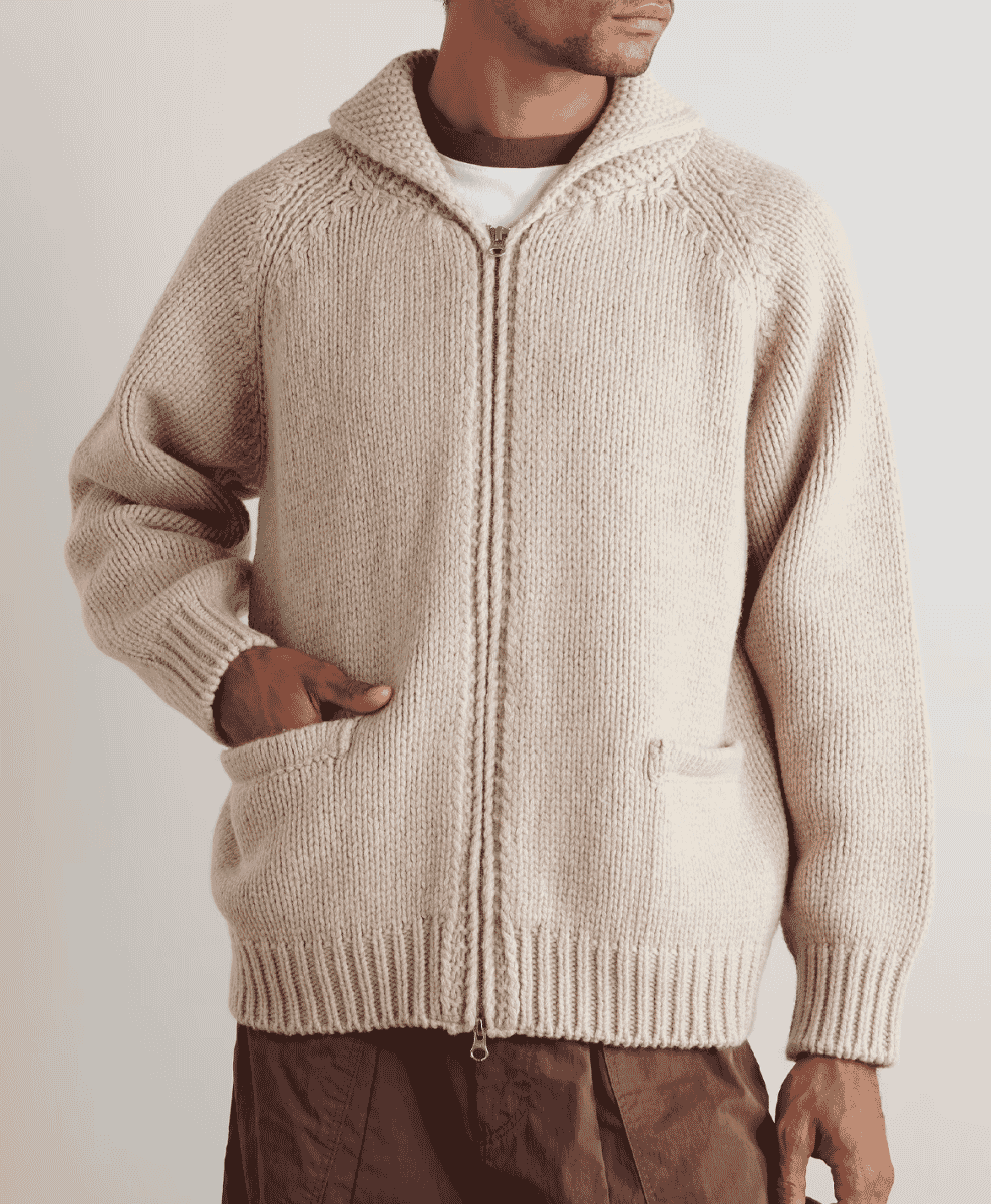 Man in a cream-colored chunky-knit zip-up cardigan with a hood and front pockets.