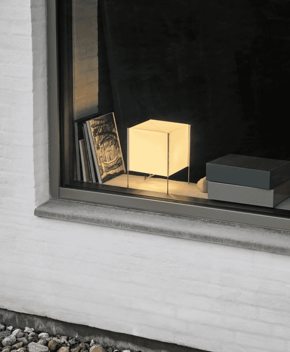A glowing cube lamp and books displayed in a minimalist window setting.