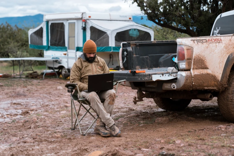 A hunter working on a laptop at a rustic campsite with the Poseidon XL power bank providing power.