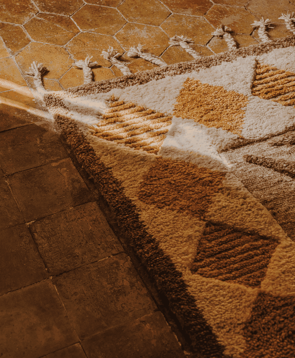 Close-up of a geometric-patterned wool rug in earthy tones on hexagonal stone tiles.