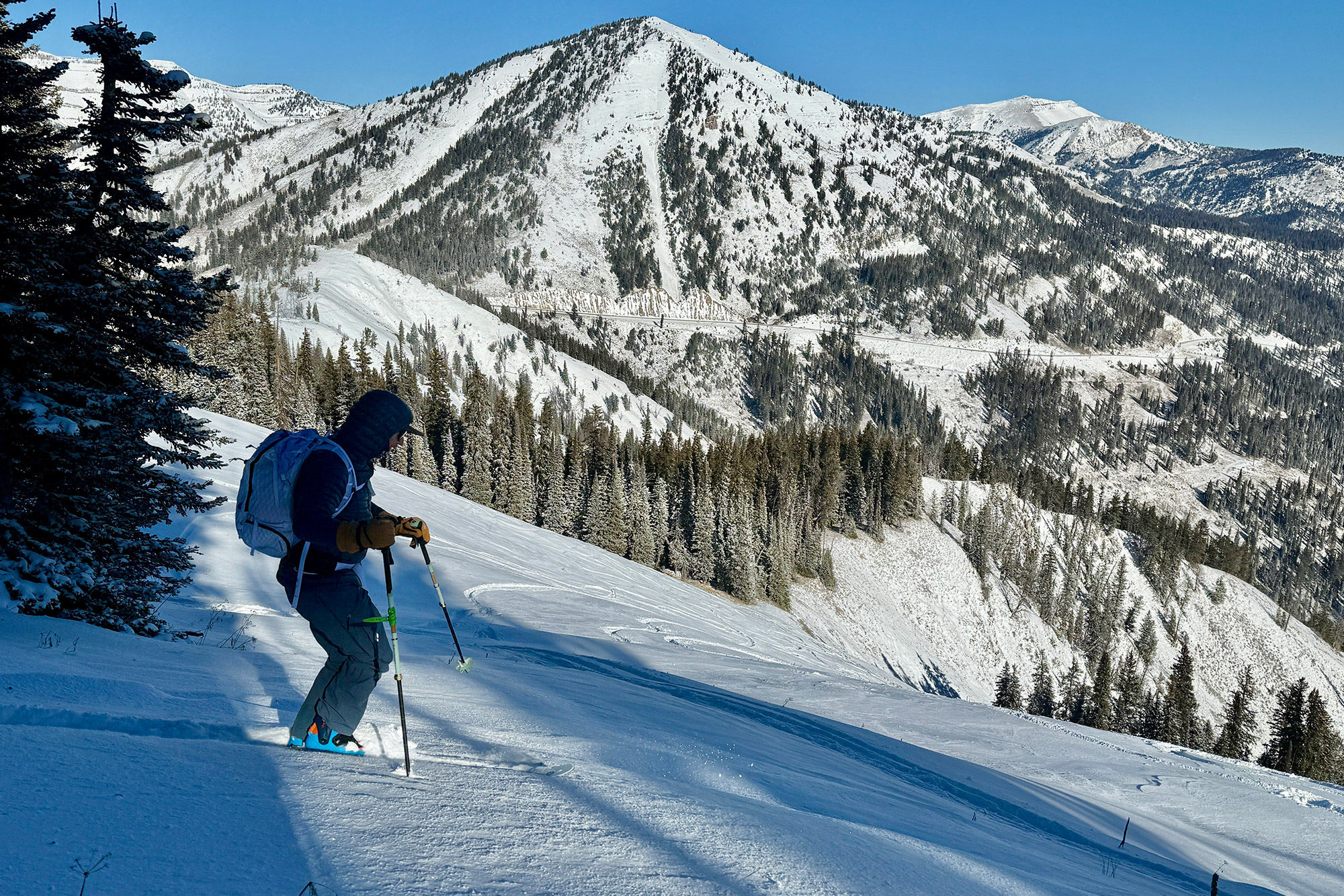 A skier standing on a ridge looking out over a massive snow-covered mountain valley.