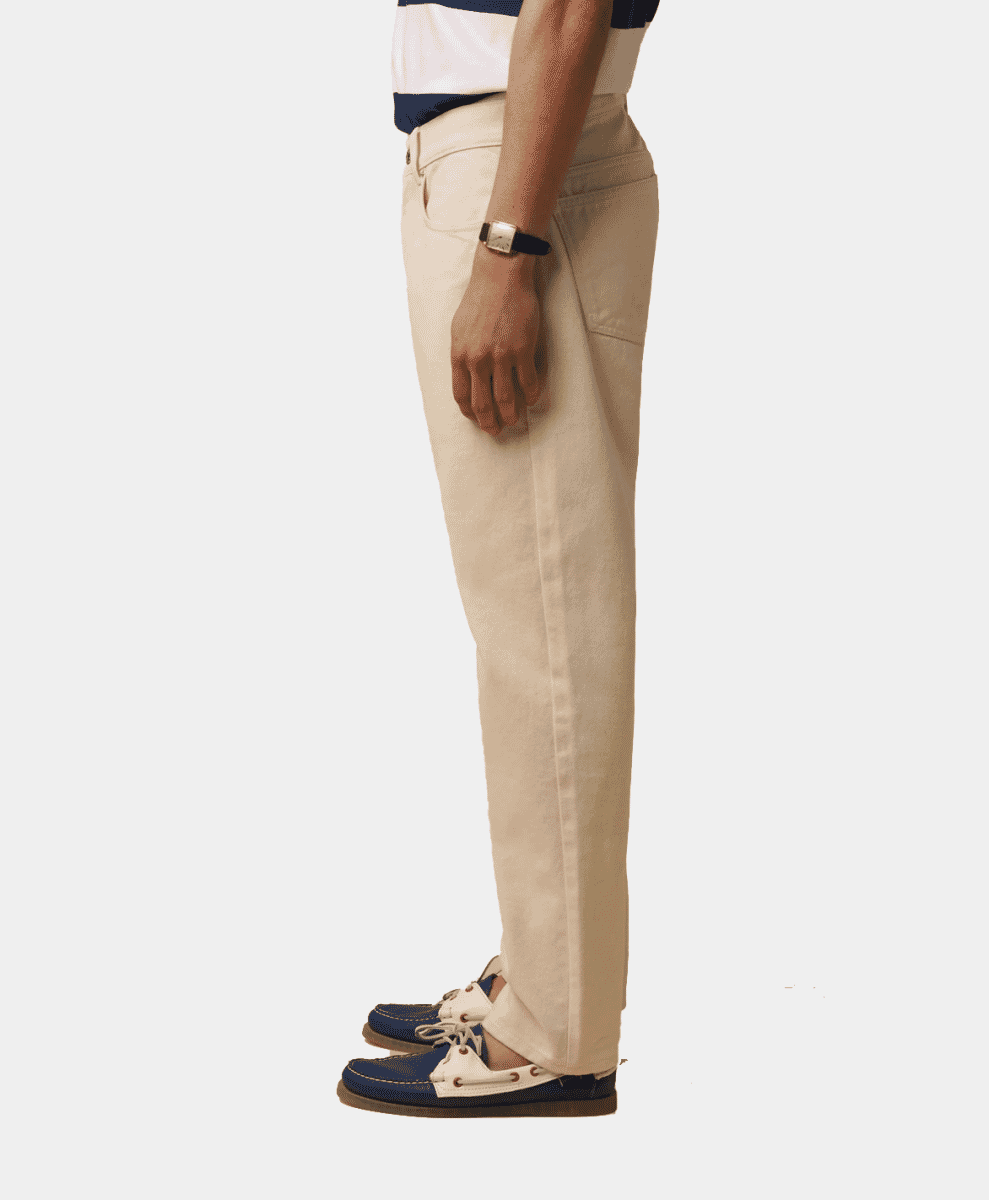 A man in profile wearing cream trousers, a striped polo, and blue-and-white boat shoes.