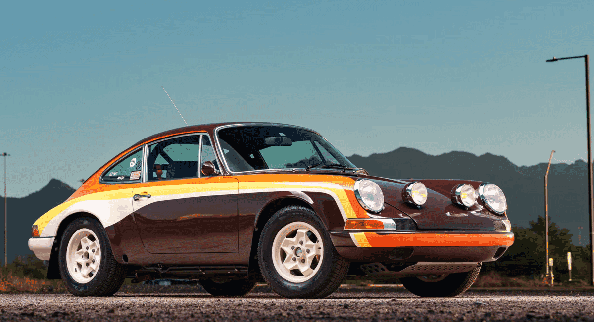 Side profile of a vintage Porsche 911 rally car with bold orange, white, and brown racing stripes.