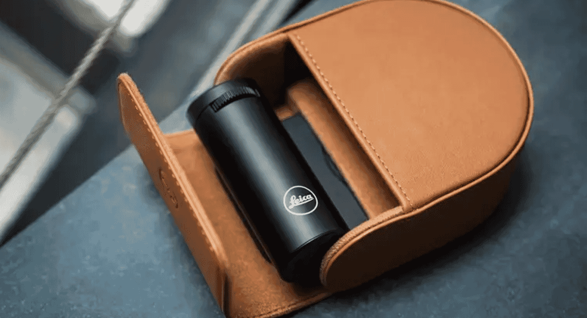 Close-up of the Leica optical device and its tan leather case on a textured surface.