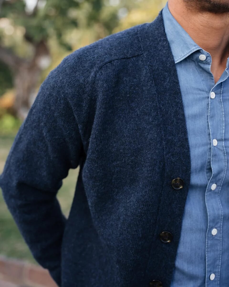 Close-up of a navy blue shawl collar knit cardigan worn over a light blue Oxford shirt.