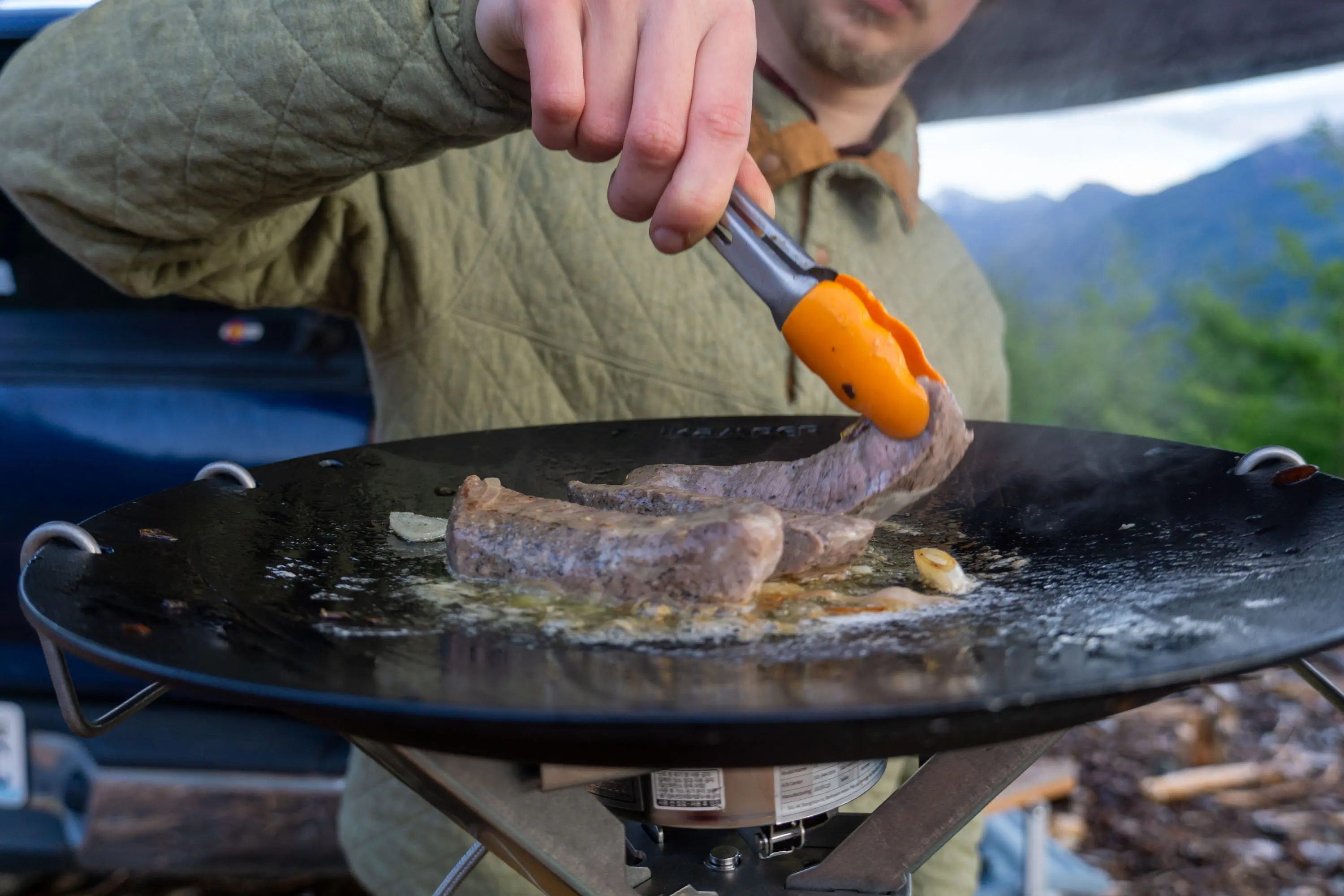 Steaks searing on a high-heat camping grill outdoors.