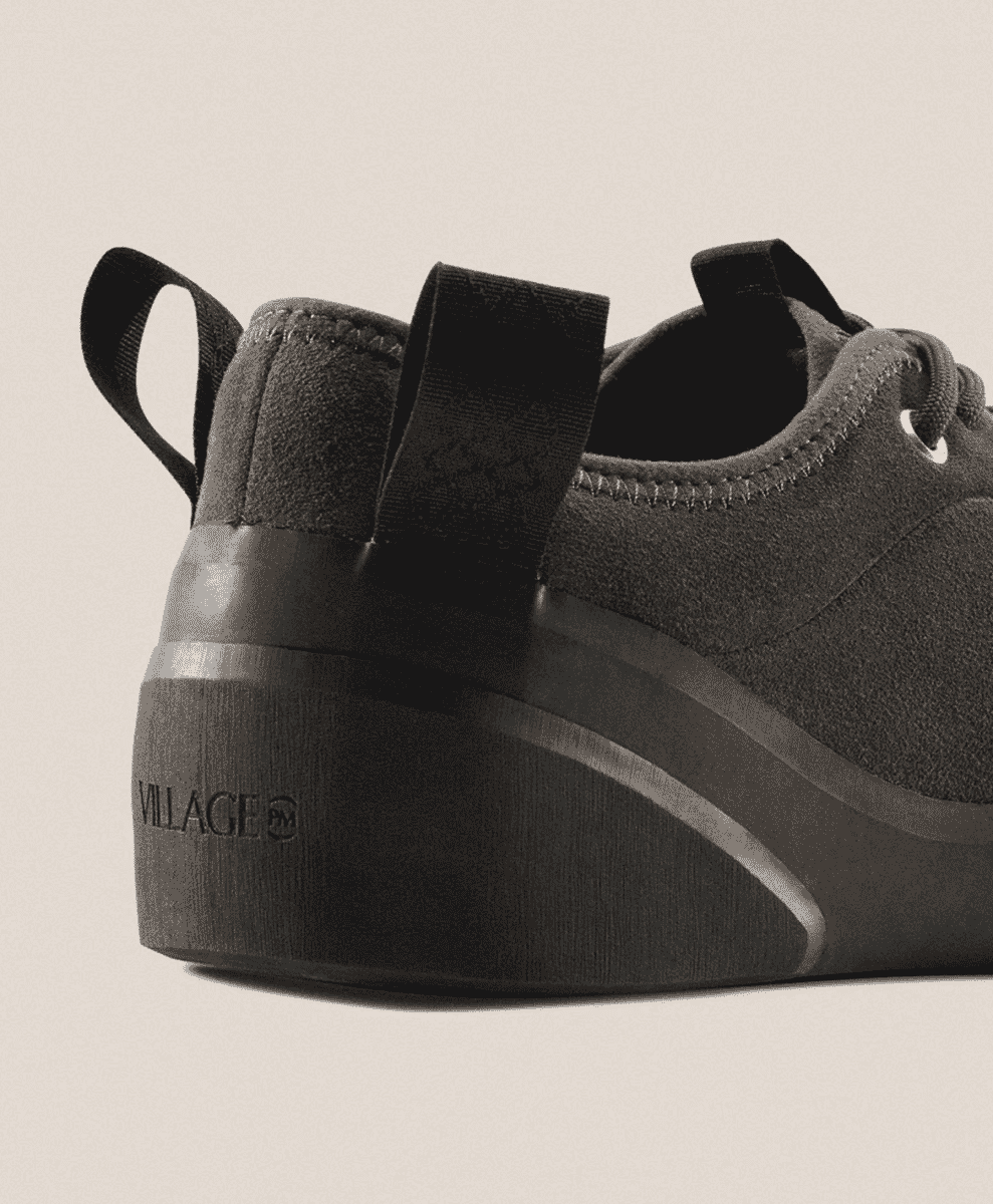 Close-up of a black suede sneaker focusing on the chunky sole with VILLAGE PM branding.