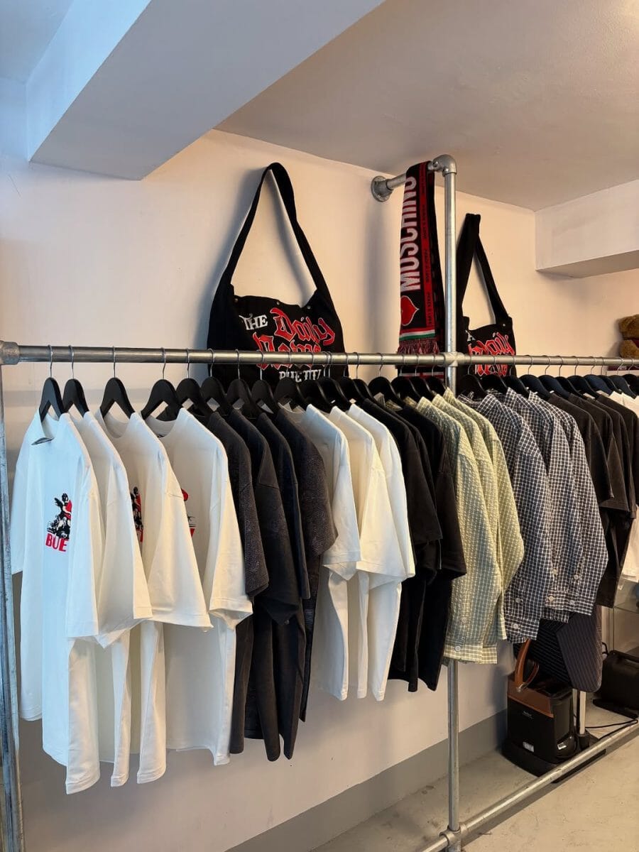 Industrial clothing rack displaying white and black graphic t-shirts and branded tote bags.